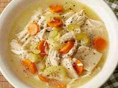 a white bowl filled with chicken and carrots on top of a wooden tablecloth