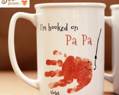 two coffee mugs with handprinted images on them, one is red and the other is white