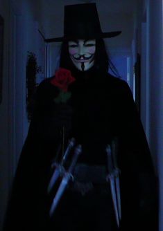 a person wearing a mask and holding two large knives in the dark with a rose on their forehead