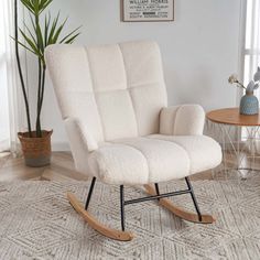 a white rocking chair sitting on top of a rug next to a potted plant