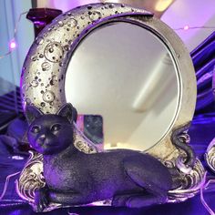 a cat figurine sitting in front of a mirror on top of a table