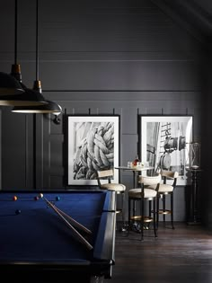 a pool table and chairs in a room with pictures on the wall above it, along with two bar stools