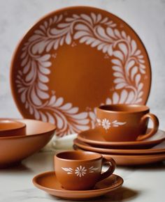 an orange dinnerware set with white designs on the plates and cups is sitting on a marble surface