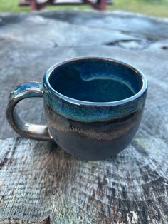 a blue cup sitting on top of a wooden table next to a bench in the background