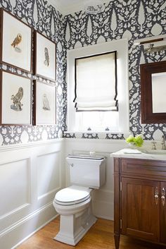 a white toilet sitting in a bathroom next to a sink and window with pictures on the wall