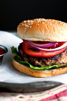 a hamburger with lettuce, tomato and onion on it next to a small bowl of ketchup