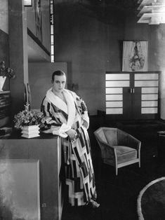 an old photo of a woman in a kimono standing next to a table and chair