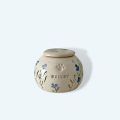 a white ceramic jar with blue flowers painted on the front and bottom, that says bailey