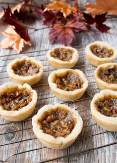 several small pies sitting on top of a wire rack next to leaves and autumn leaves