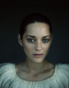 a woman with blue eyes wearing a white dress and looking at the camera while standing in front of a dark background