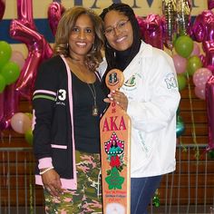 two women standing next to each other in front of balloons and balloon arch holding up a skateboard