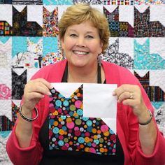 a woman holding up a piece of paper in front of a quilt