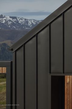 the side of a black building with mountains in the backgrouds and snow on top