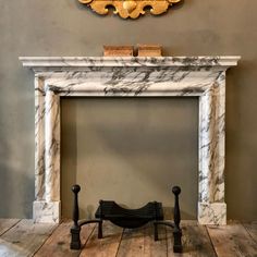 an antique fireplace with marble mantle and gold leaf decoration on the wall above it in a living room