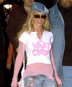 a woman in jeans and a pink shirt is walking through the street with her hat on