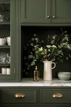 a vase filled with flowers sitting on top of a counter next to green cupboards