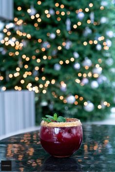 a drink in a glass sitting on top of a table next to a christmas tree