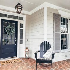 two chairs sitting on the front porch of a house with blue doors and shutters