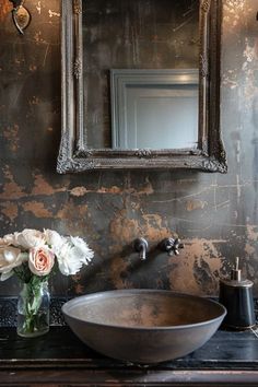 a bathroom sink sitting under a mirror next to a vase with white flowers in it