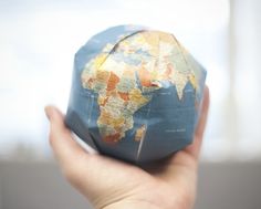 a person holding up a small globe in their hand with the world map on it