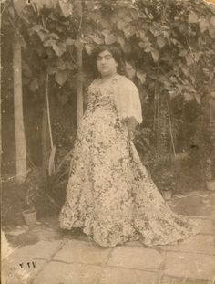 an old photo of a woman in a long dress standing next to a wall with ivy growing on it