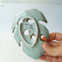 a hand holding a ceramic object with holes in it's center and writing on the side