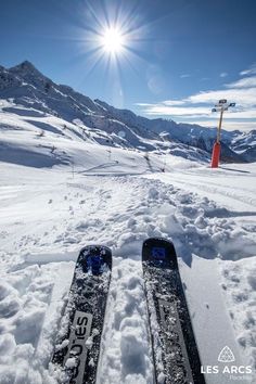 pair of skis sitting in the snow on top of a mountain with sun shining behind them