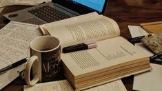 an open book sitting on top of a wooden table next to a laptop and coffee cup