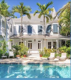 a large white house with palm trees surrounding it and a swimming pool in the foreground