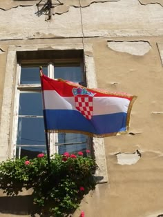 two flags flying in front of a window with flowers on the windowsill and an old building