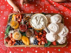 a platter filled with fruit and dips on top of a red table cloth