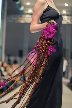 a woman is walking down the runway in a black dress with purple flowers on it