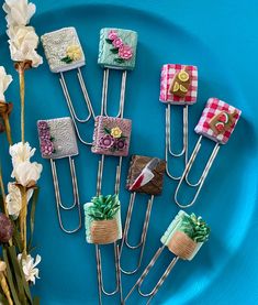 several pins with different designs on them sitting on a blue plate next to some flowers