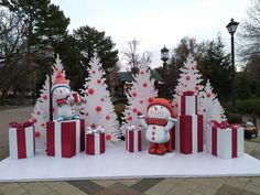 two snowmen are standing in front of christmas trees and presents on a white table