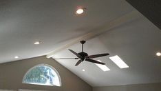 a ceiling fan in the middle of a room with two windows and a vaulted ceiling