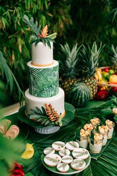 a wedding cake with tropical leaves and pineapples on the top is surrounded by other desserts