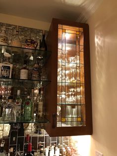 a cabinet with many bottles and glasses on it in a room that has glass shelves