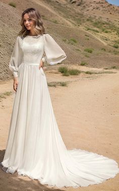 a woman in a long white dress standing on the dirt road with her arms behind her back