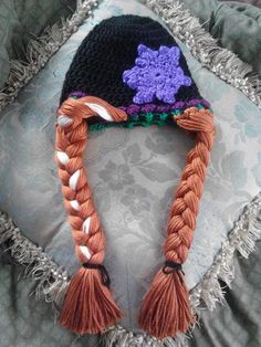 a knitted hat with braids and flowers on the top is laying on a pillow