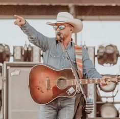 a man with a cowboy hat and glasses playing an acoustic guitar at a music festival