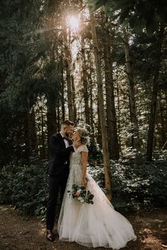 a bride and groom standing in the woods at their wedding day with sun shining through the trees