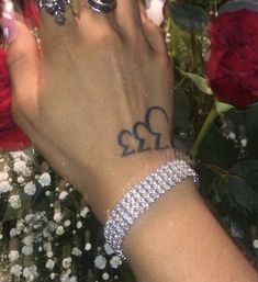 a woman's hand with two hearts tattooed on it and flowers in the background