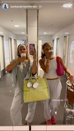 two women taking pictures with their cell phones in an office building, one holding a bag and the other carrying a purse