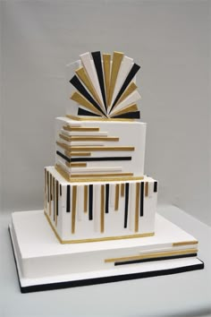 a three tiered cake with black and gold stripes on it's sides, topped by an art deco fan