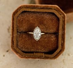 an engagement ring in a velvet box on top of a carpeted floor, with the diamond set in the center