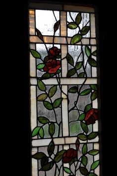 a stained glass window with red flowers and green leaves on the outside, against a dark background