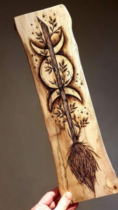 a hand holding up a wooden plaque with an image of a plant and moon on it