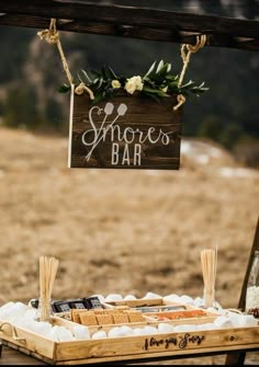 a wooden sign that says smores bar hanging from the side of a table filled with marshmallows