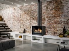 a living room filled with furniture and a fire place next to a brick wall that has stairs leading up to it