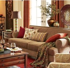 a living room filled with lots of furniture next to a window covered in red and orange pillows